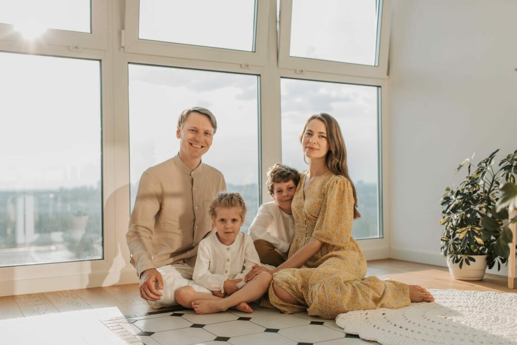 A cheerful family of four sitting together on the floor of a sunlit living room.